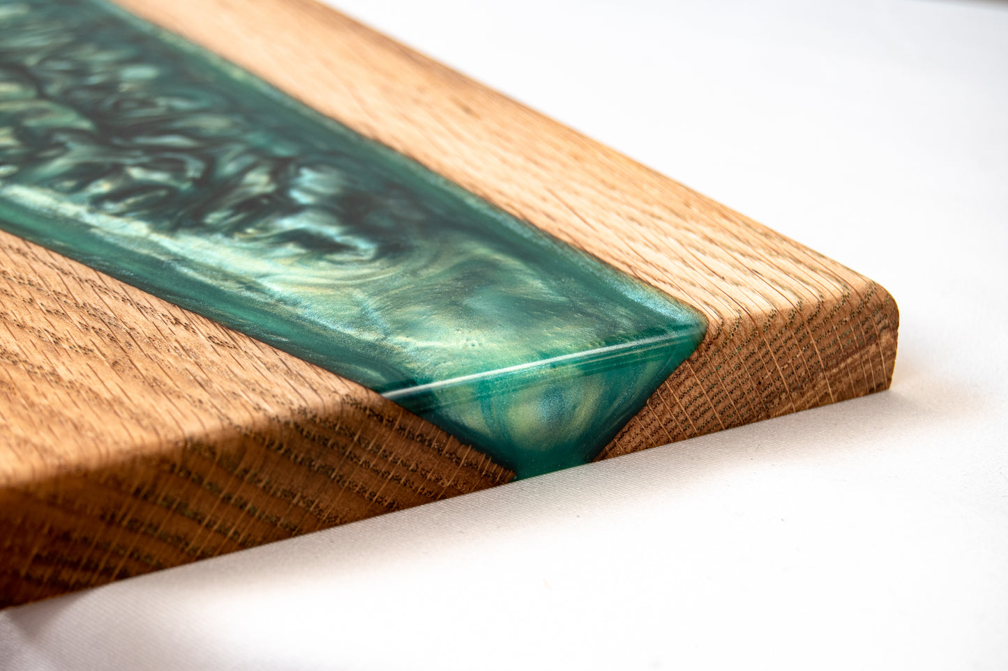 Primer plano de la esquina de una tabla de roble con resina epoxy verde, sobre una superficie blanca