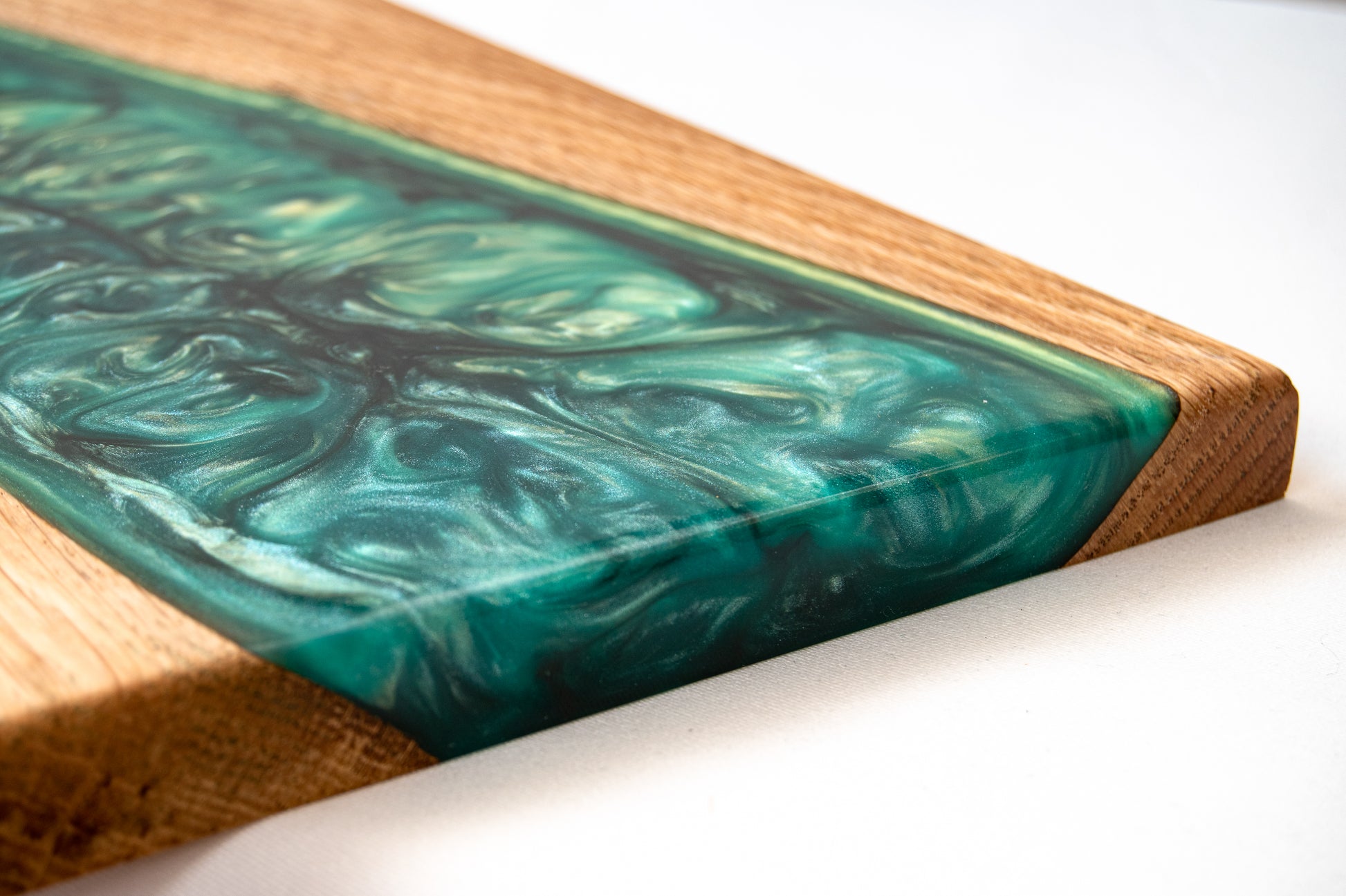Primer plano de la resina epoxy verde con efecto ondulado sobre madera de roble en una tabla de servir artesanal.