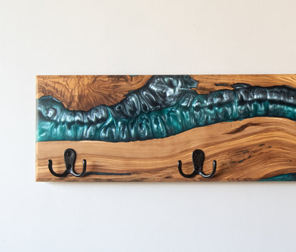 Vista de detalle de perchero de madera de olivo con resina epoxi azul turquesa en acabado tipo río y ganchos de metal negro