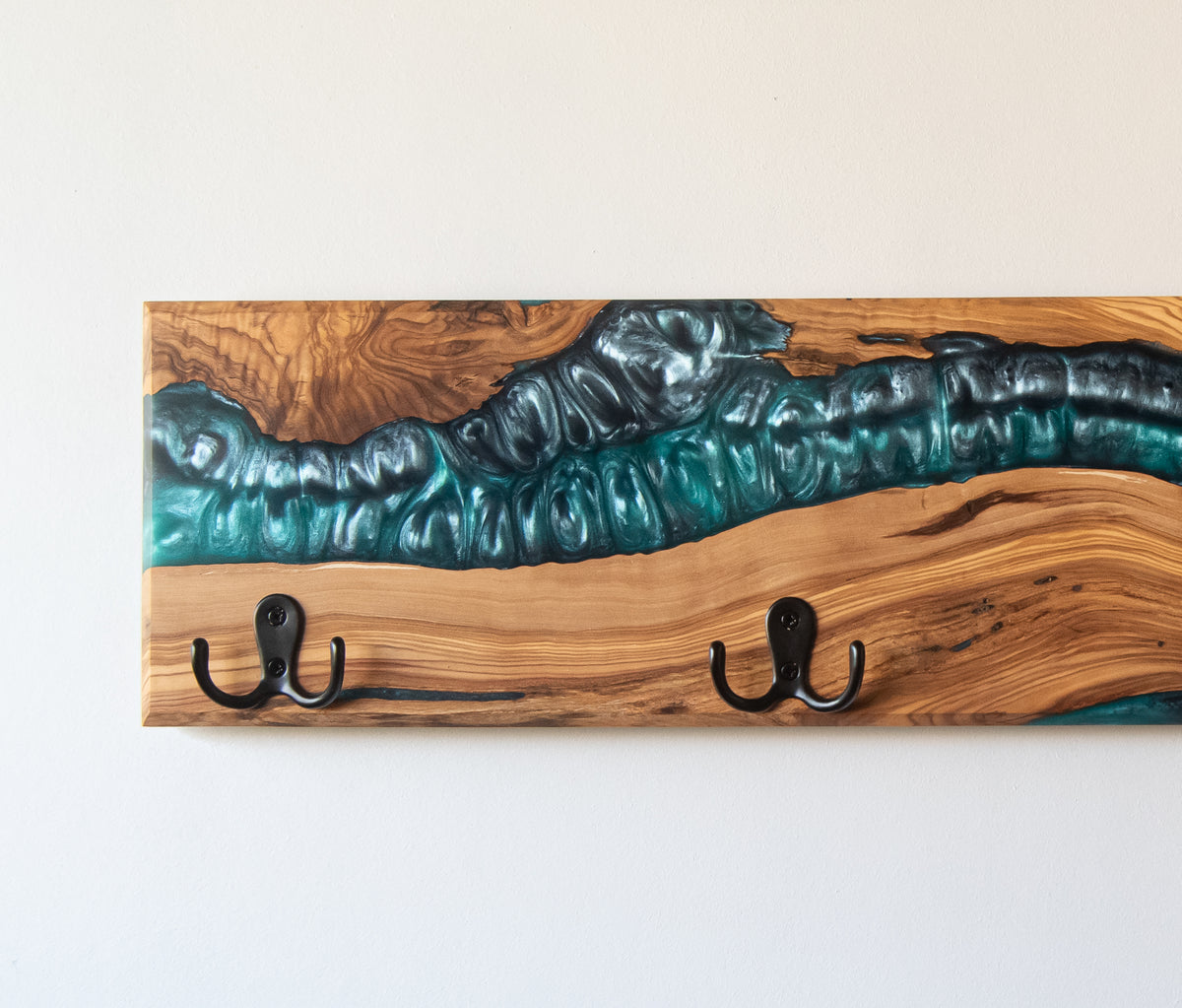 Vista de detalle de perchero de madera de olivo con resina epoxi azul turquesa en acabado tipo río y ganchos de metal negro