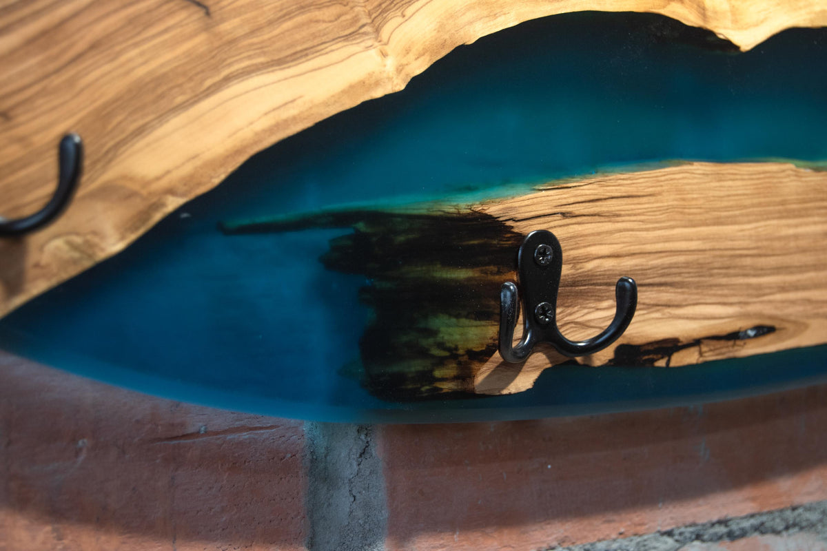 Detalle de ganchos negros y río de resina epoxi azul en perchero skate