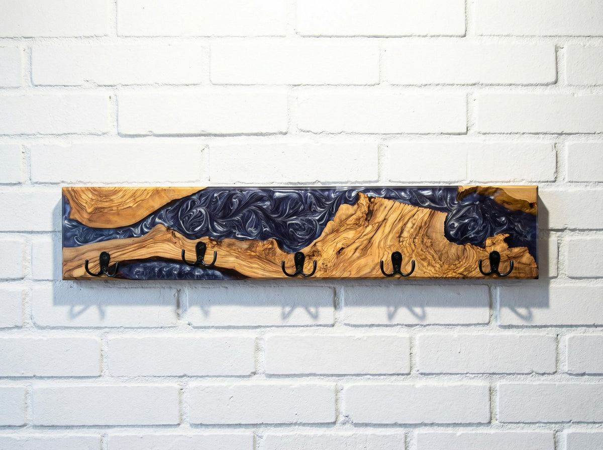 Perchero de pared artesanal en madera de olivo con resina epoxi violeta y ganchos negros, sobre pared de ladrillo blanco