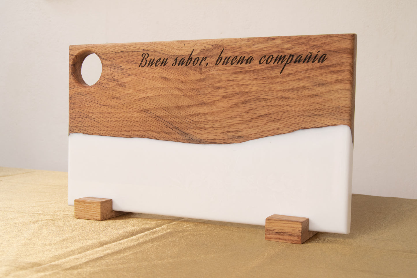 Tabla de madera de roble con resina epoxi blanca y frase grabada "Buen sabor, buena compañía", de pie sobre soportes de madera