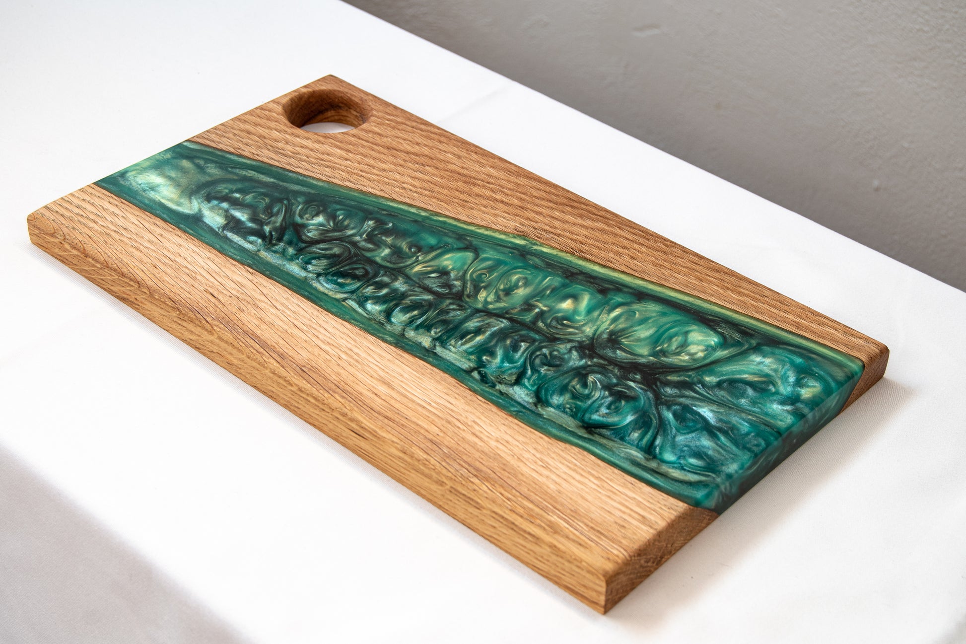 Tabla de charcutería de madera de roble con banda de resina epoxy verde, fotografiada sobre fondo gris claro