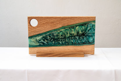 Tabla de servir de madera de roble con resina epoxy verde, colocada de pie sobre un mantel blanco