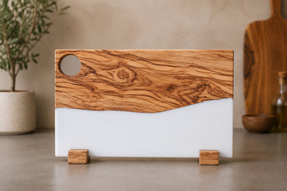 Tabla de servir de madera de olivo con veta natural y resina epoxi blanca, de pie sobre fondo neutro