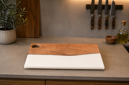 Tabla de madera de roble y resina epoxi blanca vacía sobre encimera de cocina con utensilios de fondo