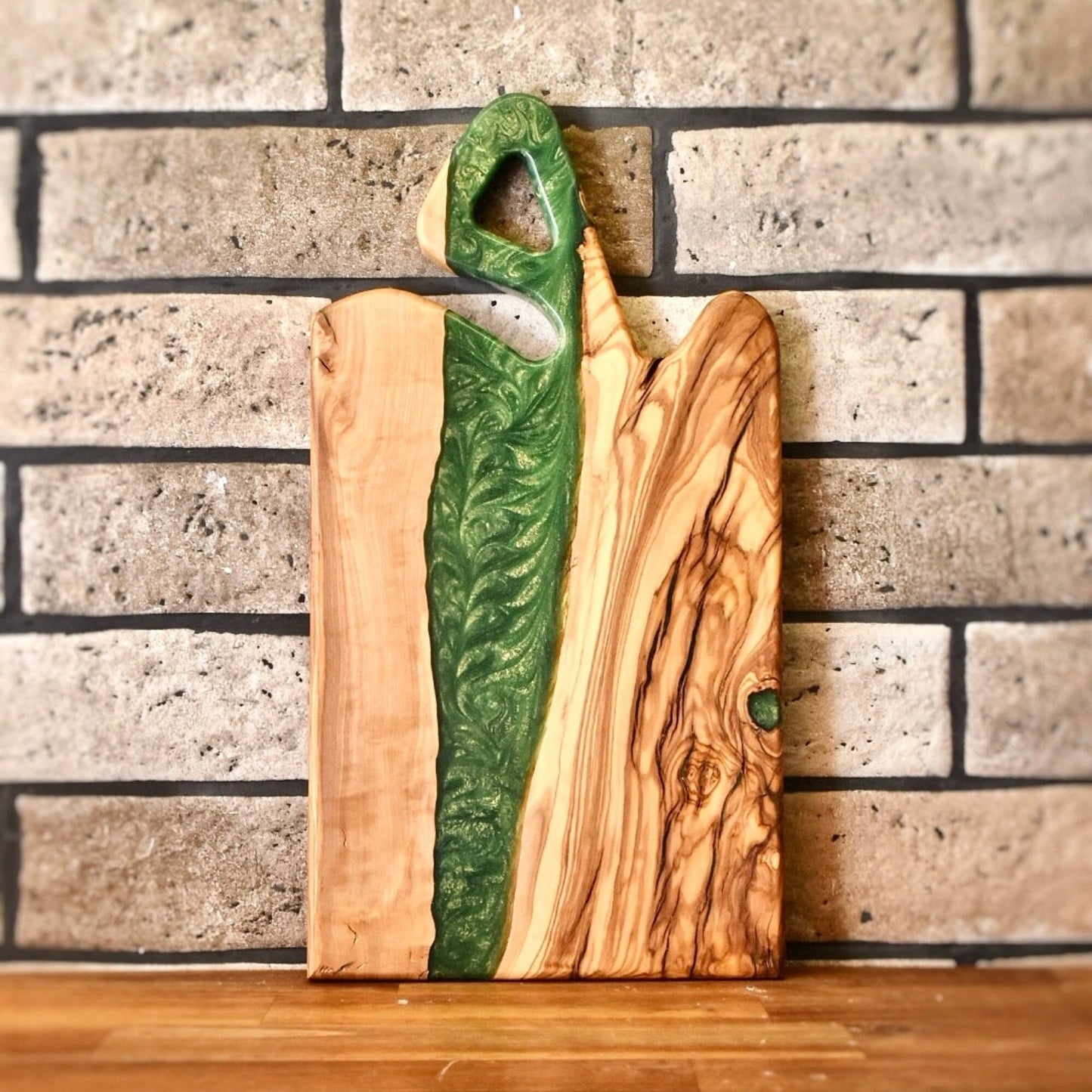 Tabla artesanal apoyada en pared de ladrillo, madera de olivo y resina verde