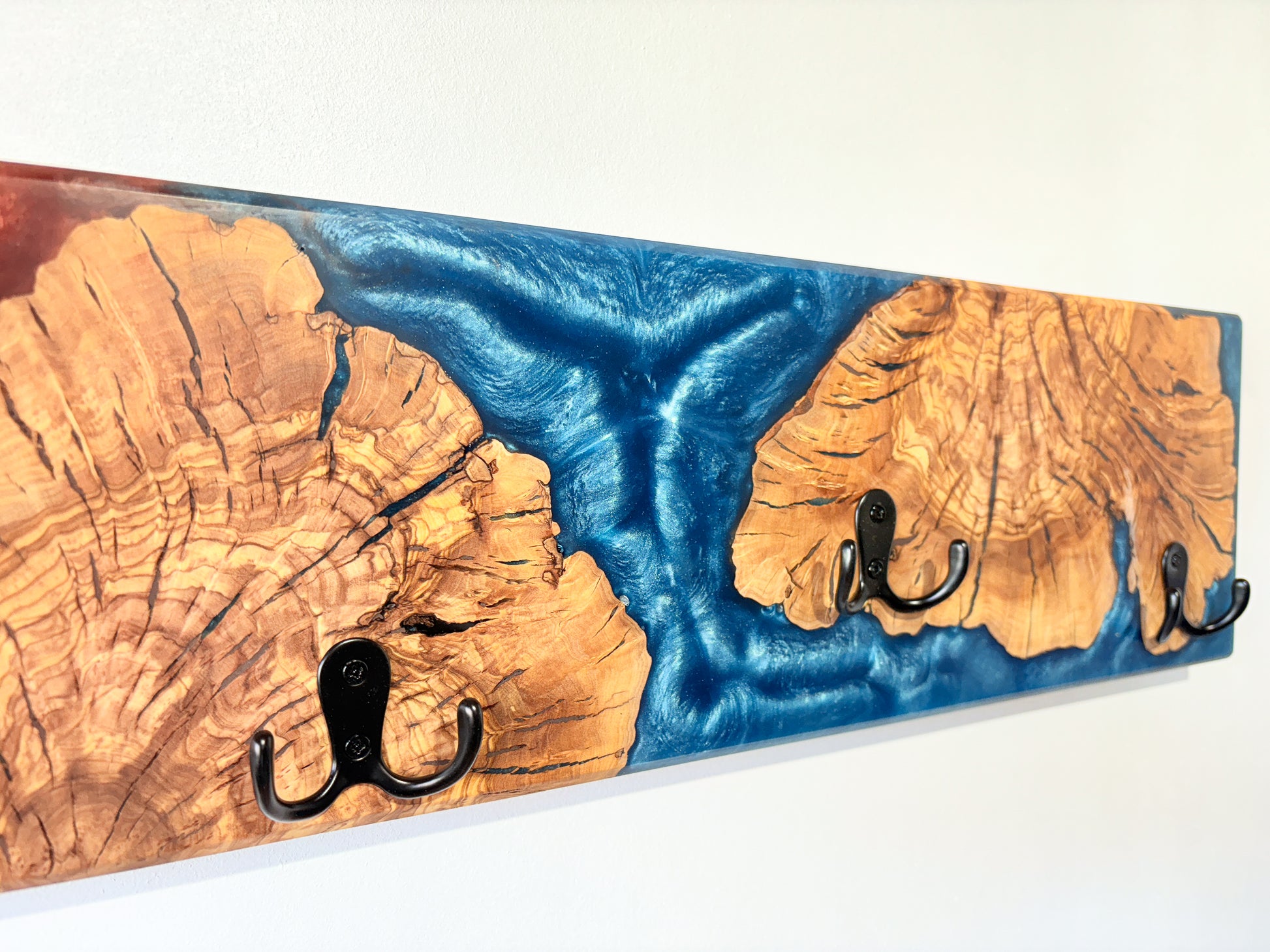 Perchero de pared en madera de olivo con detalles de resina epoxy azul y roja, pieza exclusiva