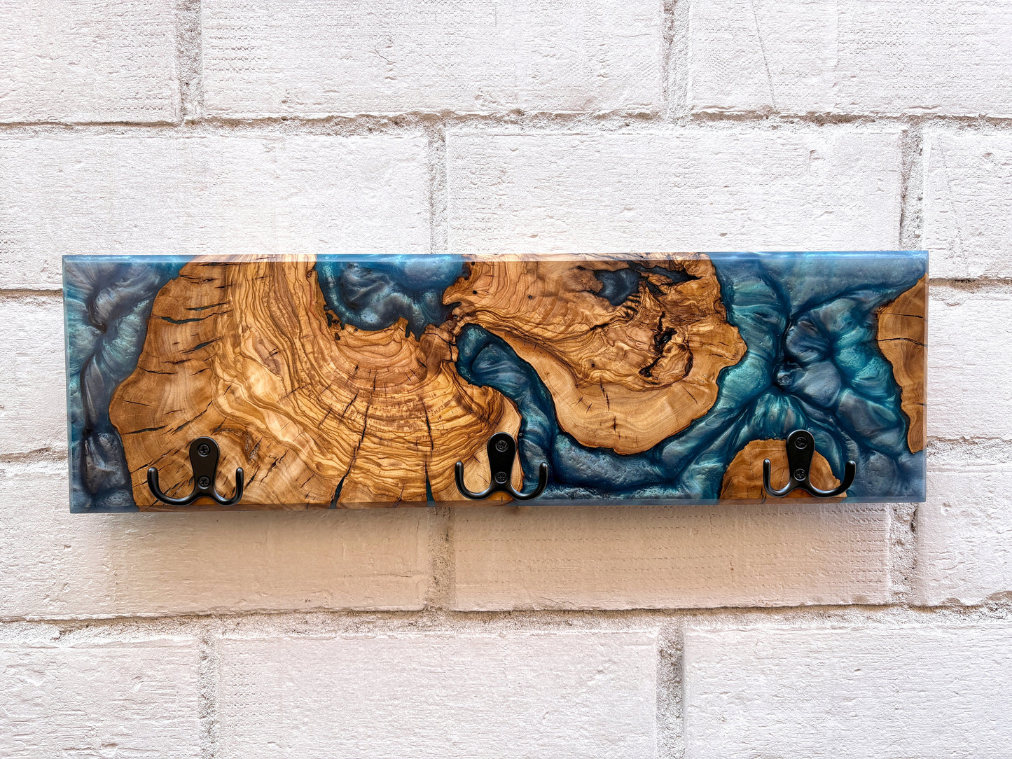 Perchero de madera de olivo con resina epoxy azul sobre pared de ladrillo