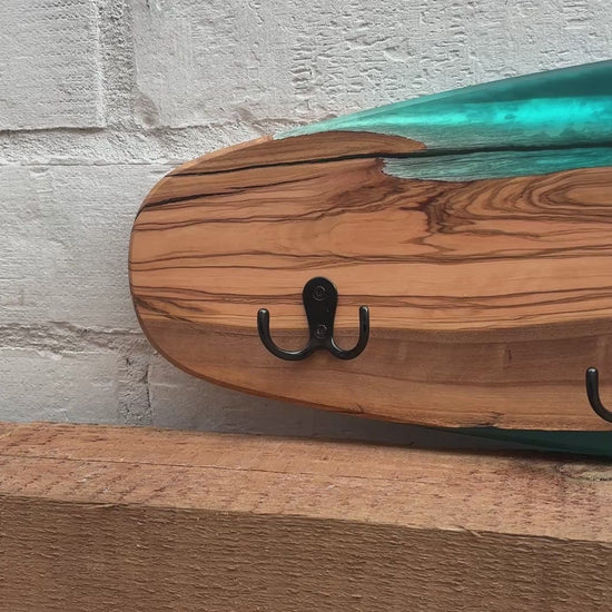 Vídeo del perchero de pared en forma de skate, madera de olivo con resina epoxi azul, mostrando el detalle de la veta y los ganchos
