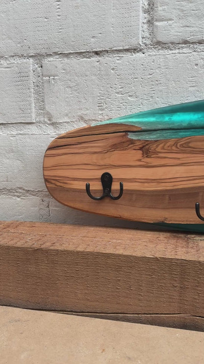Vídeo del perchero de pared en forma de skate, madera de olivo con resina epoxi azul, mostrando el detalle de la veta y los ganchos