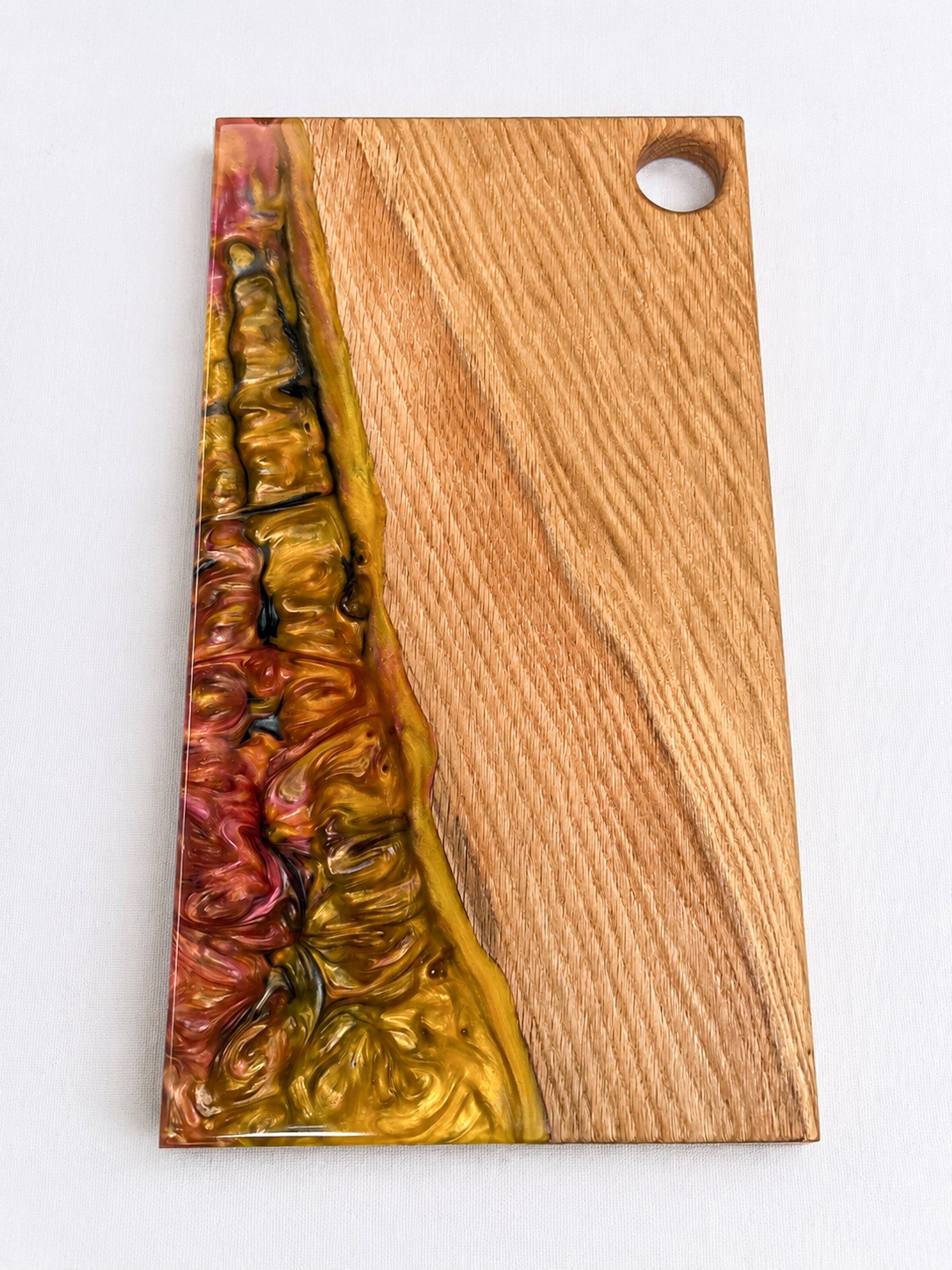 Tabla de presentación artesanal de madera de roble maciza y resina epoxi dorada y burdeos sobre fondo blanco.