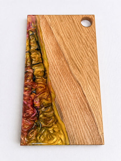 Tabla de presentación artesanal de madera de roble maciza y resina epoxi dorada y burdeos sobre fondo blanco.